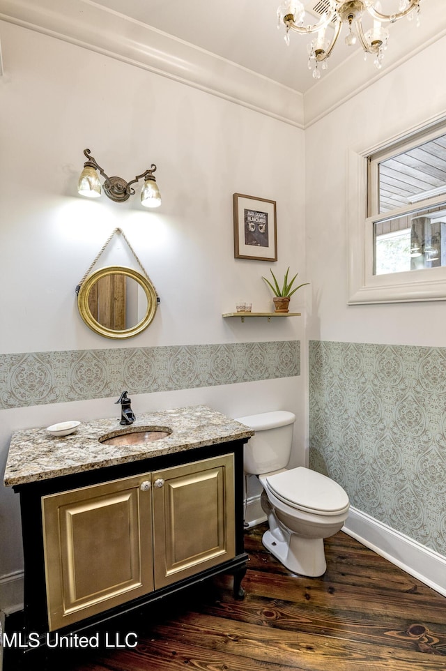 bathroom featuring toilet, a notable chandelier, wallpapered walls, wood finished floors, and vanity