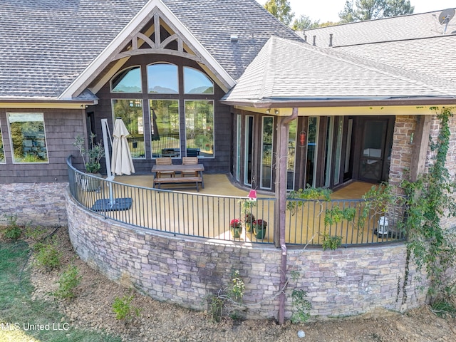 back of property featuring a shingled roof and stone siding