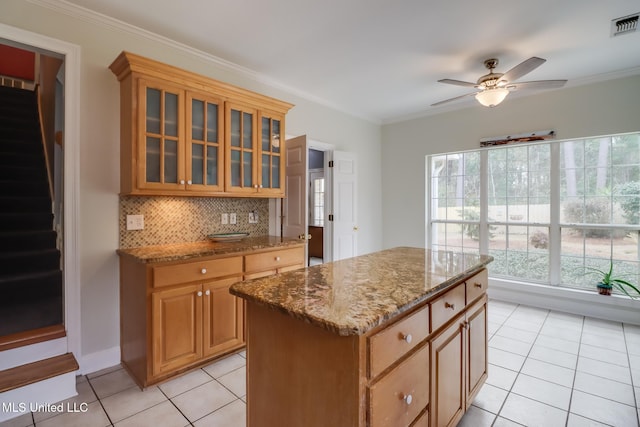 kitchen with backsplash, a kitchen island, light stone counters, ornamental molding, and light tile patterned flooring