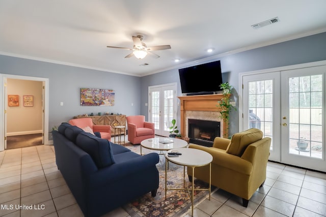 living room with french doors, crown molding, light tile patterned floors, ceiling fan, and a fireplace