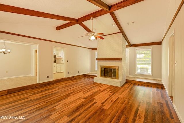 unfurnished living room featuring a brick fireplace, wood finished floors, baseboards, lofted ceiling with beams, and ceiling fan with notable chandelier