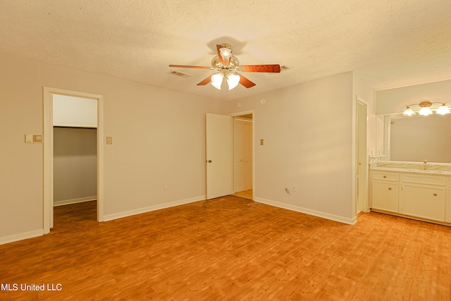 unfurnished bedroom featuring visible vents, light wood-type flooring, a textured ceiling, a spacious closet, and a sink