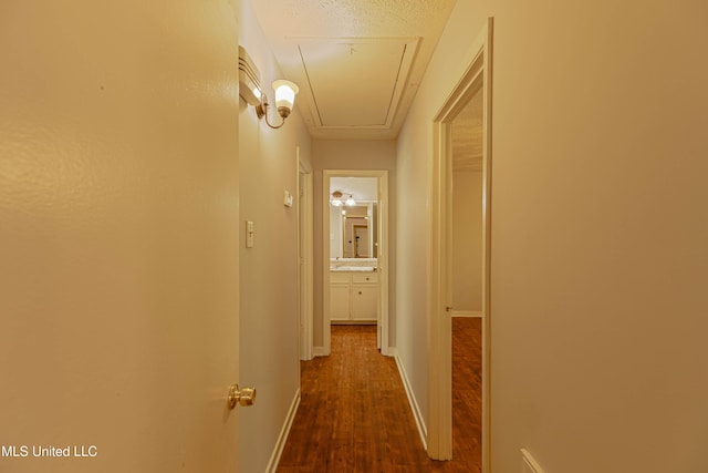 hallway with baseboards, attic access, and dark wood finished floors