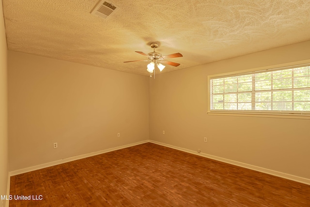spare room with ceiling fan, a textured ceiling, visible vents, baseboards, and dark wood-type flooring