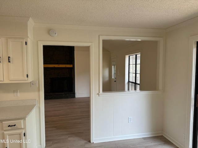 interior space with a stone fireplace, a textured ceiling, light hardwood / wood-style floors, white cabinets, and ornamental molding