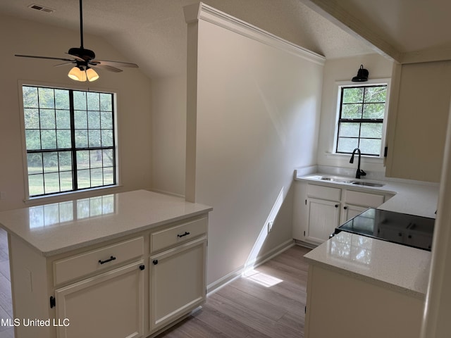 kitchen featuring white cabinets, ceiling fan, vaulted ceiling, light hardwood / wood-style flooring, and sink