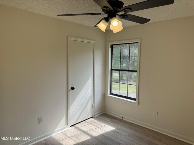 empty room featuring light wood-type flooring, a textured ceiling, plenty of natural light, and ceiling fan