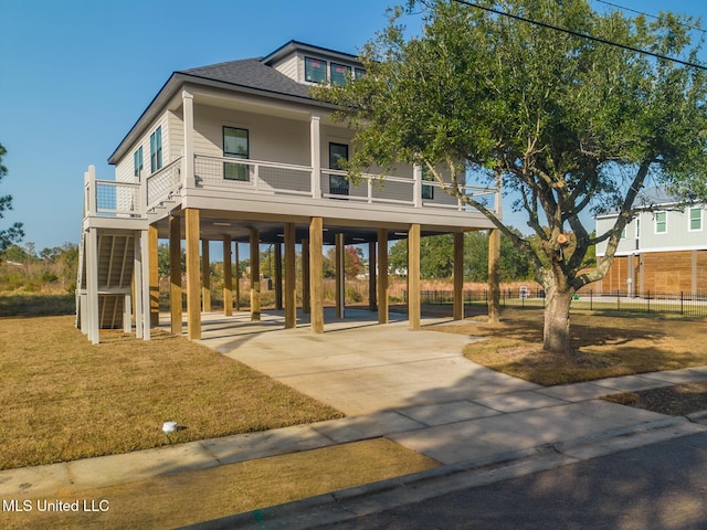 coastal inspired home featuring a front lawn, a carport, a shingled roof, and driveway