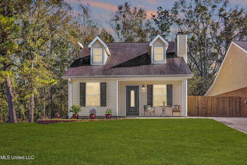 cape cod home featuring a lawn