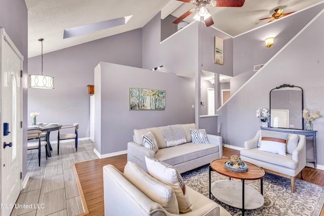 living room featuring light wood-type flooring, a skylight, high vaulted ceiling, and ceiling fan