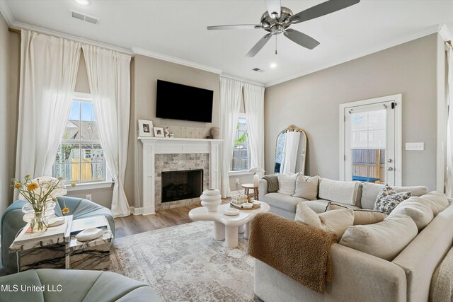 living room with a tiled fireplace, visible vents, crown molding, and wood finished floors