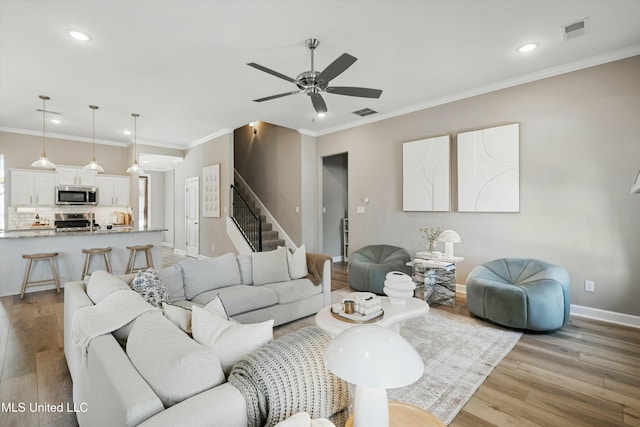 living room featuring stairway, light wood-style flooring, visible vents, and baseboards