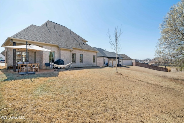 back of house with fence, a yard, a shingled roof, brick siding, and a patio area