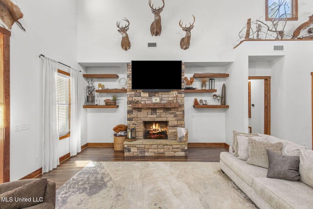 living room with a stone fireplace, wood finished floors, visible vents, and baseboards