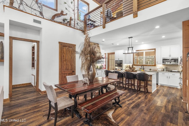 dining area with dark wood-type flooring, visible vents, plenty of natural light, and a high ceiling