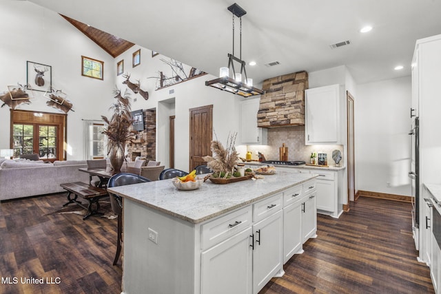 kitchen featuring visible vents, decorative backsplash, dark wood-type flooring, light stone countertops, and wall chimney range hood