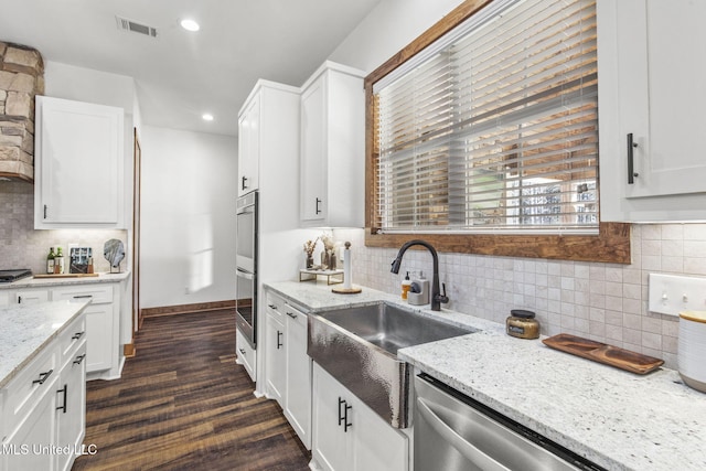 kitchen featuring light stone countertops, visible vents, white cabinets, and a sink