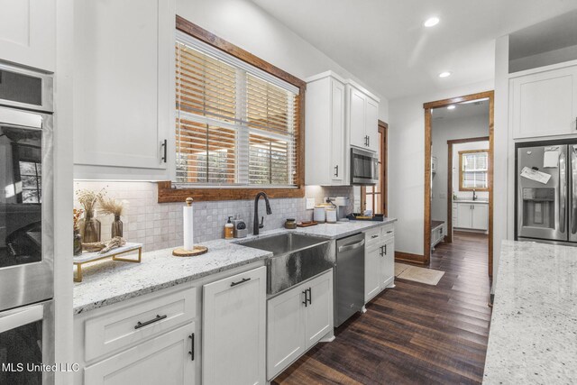 kitchen with decorative backsplash, white cabinets, appliances with stainless steel finishes, dark wood-style flooring, and a sink