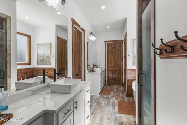 bathroom with a wainscoted wall, recessed lighting, a soaking tub, vanity, and wood finished floors