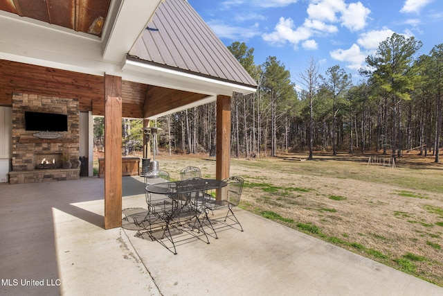 view of patio featuring an outdoor stone fireplace, outdoor dining area, and a wooded view