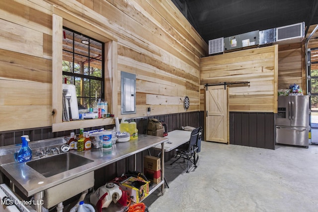 kitchen featuring stainless steel refrigerator with ice dispenser, a barn door, a sink, wooden walls, and electric panel