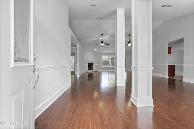 entryway with a fireplace with raised hearth, dark wood-style flooring, visible vents, vaulted ceiling, and ornate columns