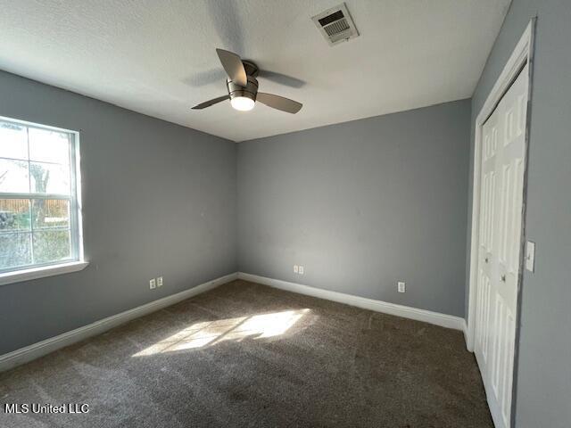 unfurnished bedroom with dark colored carpet, ceiling fan, a textured ceiling, and a closet