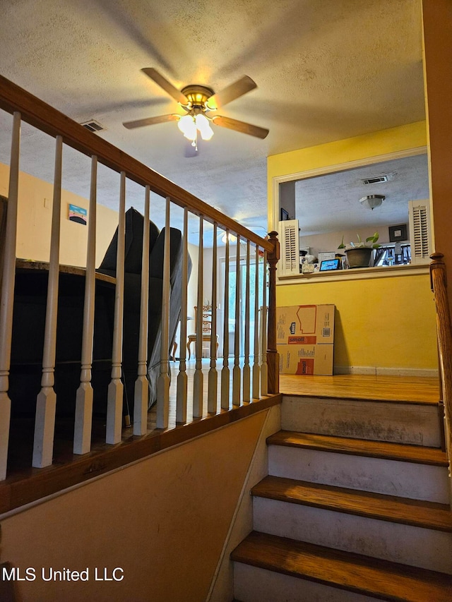 stairway featuring a textured ceiling and ceiling fan