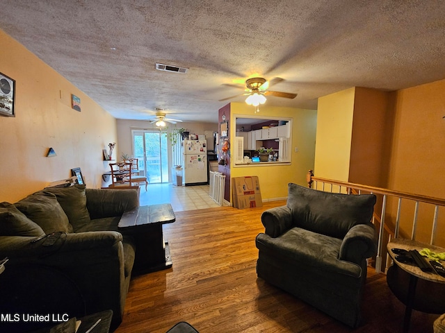 living room with a textured ceiling, wood-type flooring, and ceiling fan