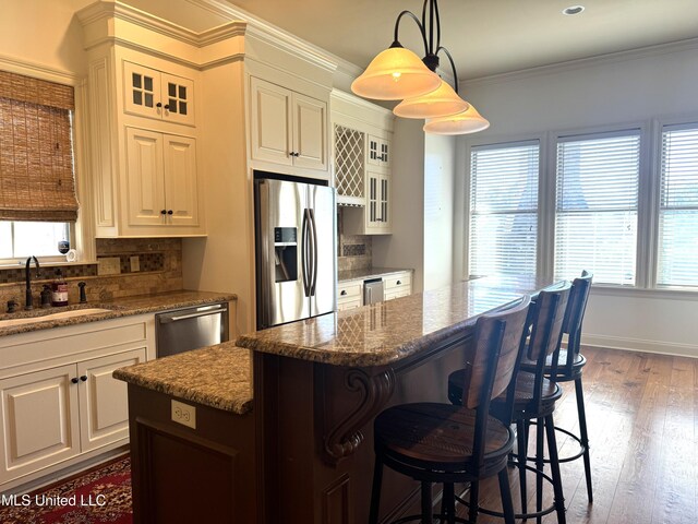 kitchen featuring stainless steel appliances, a kitchen island, light stone countertops, sink, and dark wood-type flooring