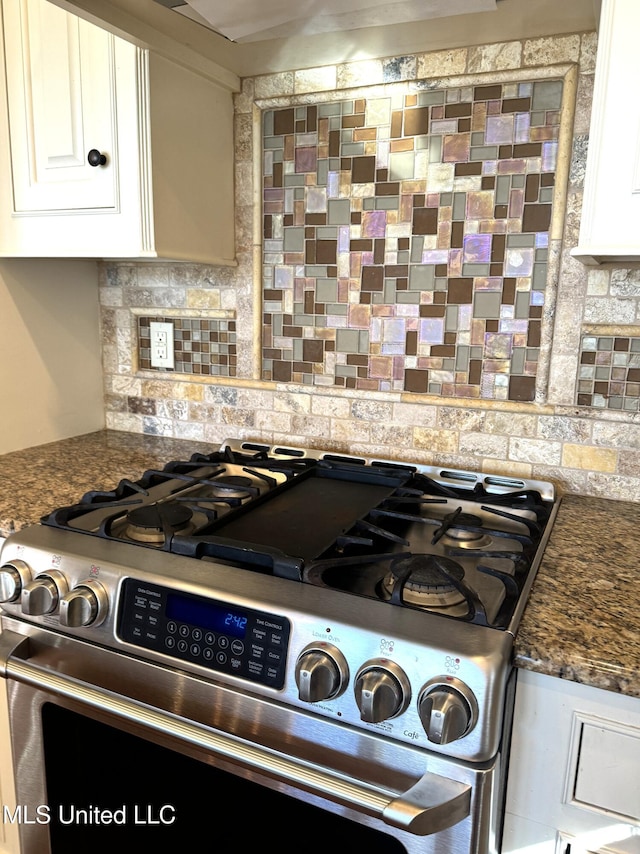 kitchen featuring white cabinets, decorative backsplash, dark stone countertops, and stainless steel gas range oven