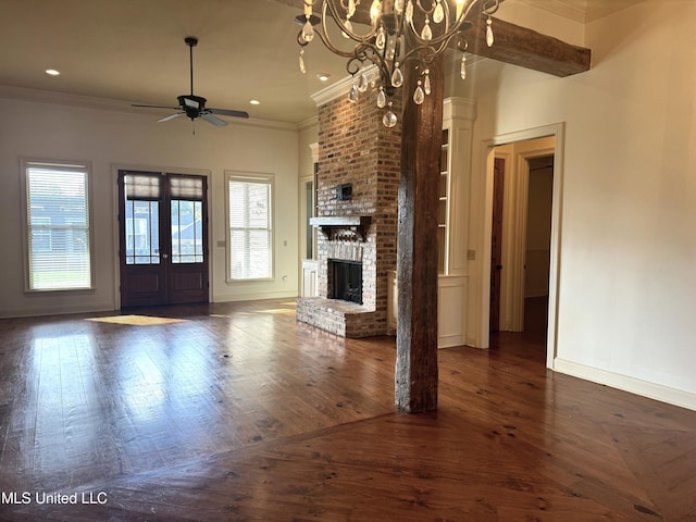 unfurnished living room with ceiling fan with notable chandelier, crown molding, dark wood-type flooring, french doors, and a brick fireplace