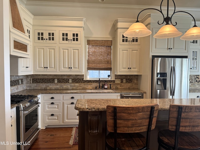 kitchen featuring sink, a breakfast bar area, appliances with stainless steel finishes, decorative light fixtures, and dark stone countertops
