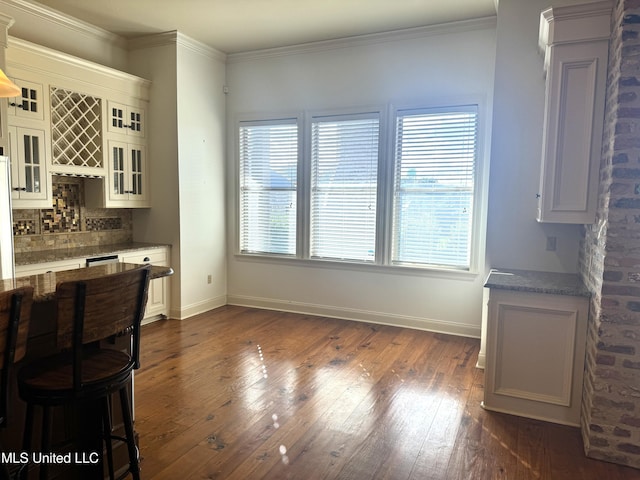 dining room with bar area, dark wood-type flooring, ornamental molding, and decorative columns