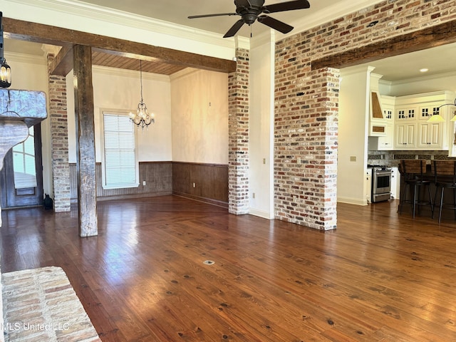 unfurnished living room featuring dark wood-type flooring, brick wall, ceiling fan with notable chandelier, and crown molding