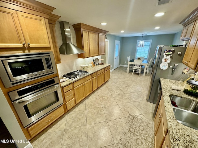 kitchen featuring backsplash, appliances with stainless steel finishes, a sink, wall chimney range hood, and light stone countertops