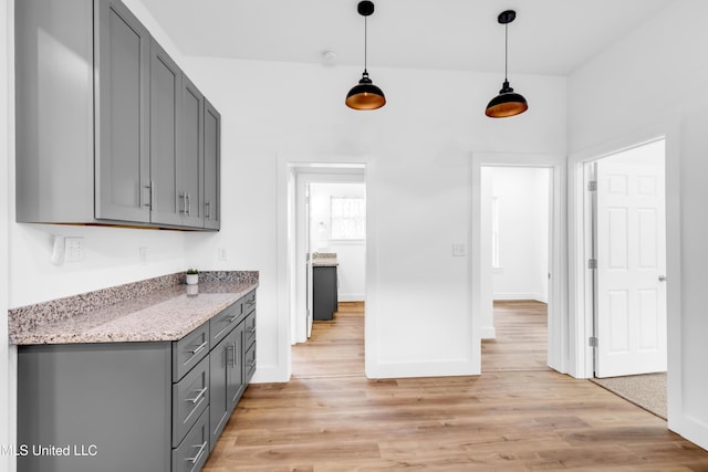 kitchen with gray cabinetry, light wood-type flooring, baseboards, light stone counters, and decorative light fixtures