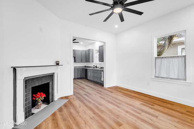 unfurnished living room with ceiling fan, a fireplace, baseboards, light wood-style floors, and recessed lighting