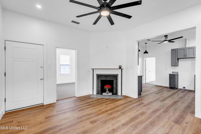 unfurnished living room featuring ceiling fan, light wood-type flooring, a brick fireplace, baseboards, and recessed lighting