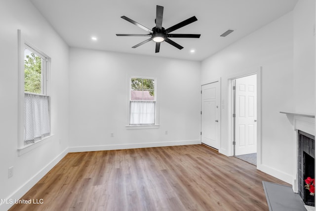 unfurnished living room with a fireplace with raised hearth, light wood-style floors, ceiling fan, recessed lighting, and baseboards