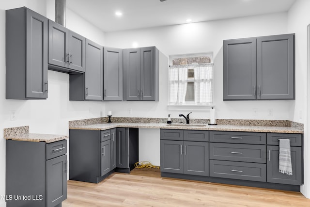 kitchen with a sink, gray cabinetry, light wood-style floors, recessed lighting, and light stone counters
