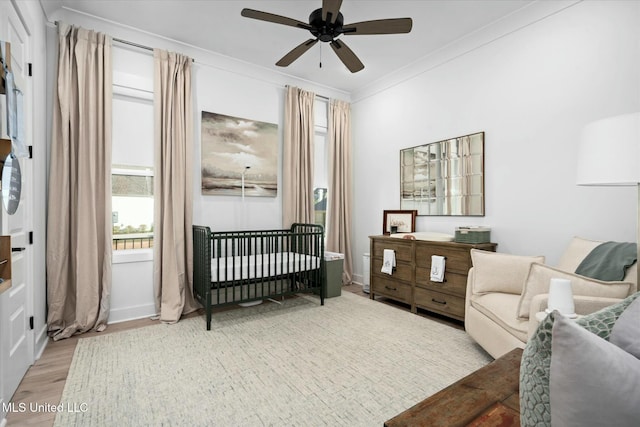 bedroom with ceiling fan, a crib, crown molding, and light hardwood / wood-style flooring