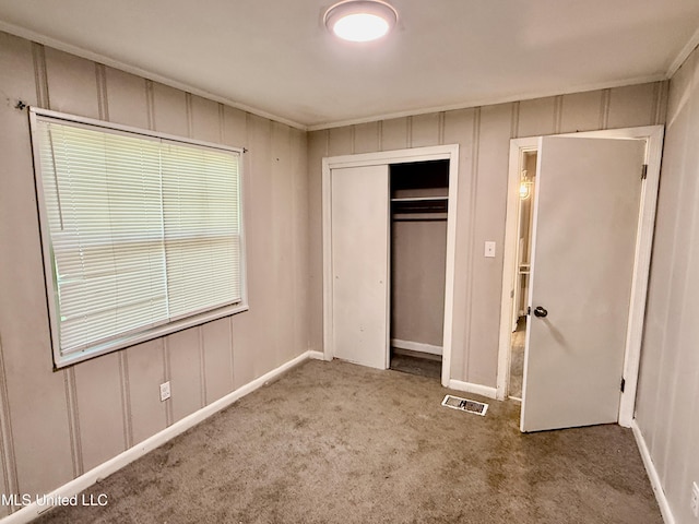 unfurnished bedroom with a decorative wall, a closet, ornamental molding, carpet, and visible vents
