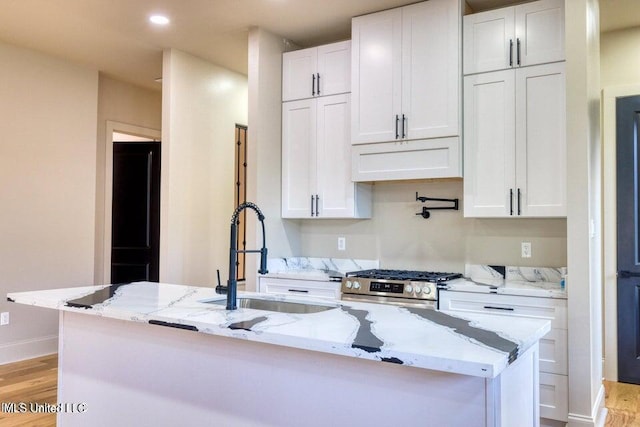 kitchen with stainless steel range with gas cooktop, light stone countertops, an island with sink, and white cabinets