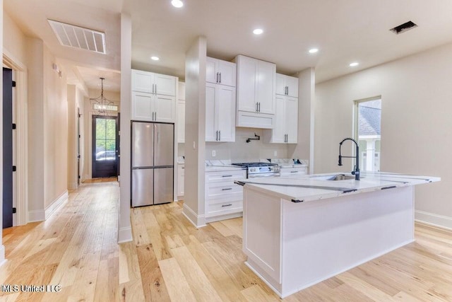 kitchen featuring an island with sink, white cabinets, light hardwood / wood-style floors, stainless steel appliances, and light stone countertops