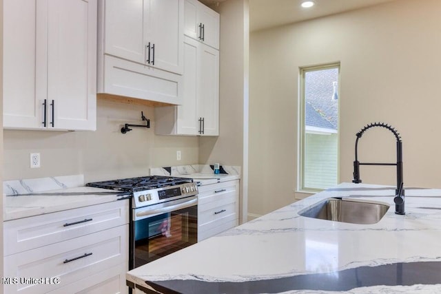 kitchen with stainless steel gas range, sink, and white cabinets