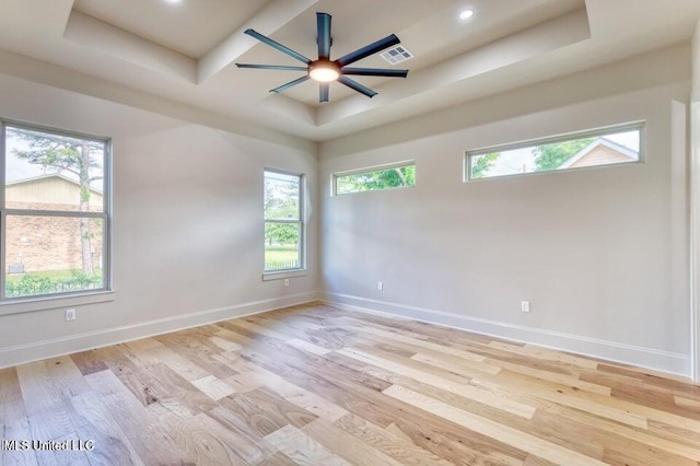 empty room featuring a tray ceiling, ceiling fan, and light wood-type flooring