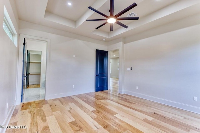 unfurnished room with ceiling fan, a tray ceiling, and light hardwood / wood-style flooring