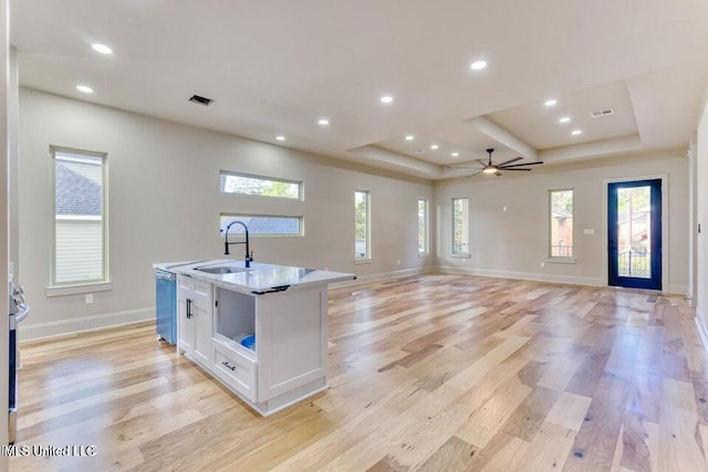 kitchen featuring white cabinetry, stainless steel dishwasher, a kitchen island with sink, a raised ceiling, and light hardwood / wood-style floors