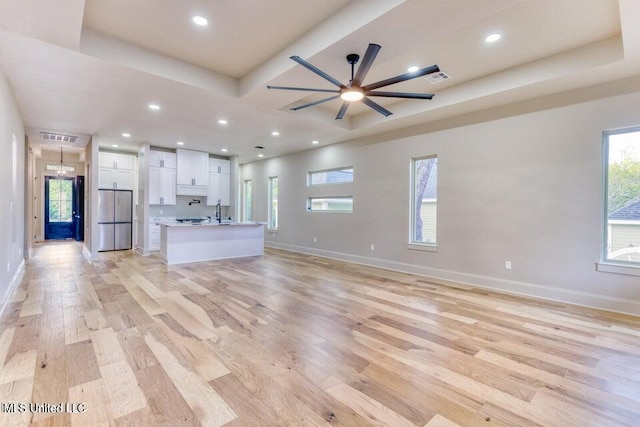 unfurnished living room featuring a raised ceiling, ceiling fan, and light wood-type flooring